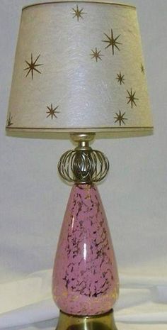 a pink and gold table lamp with a white shade on the top, sitting against a white background