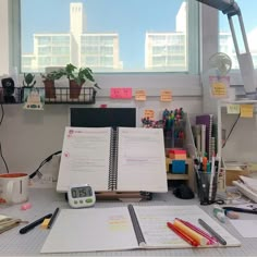 an office desk is cluttered with papers, pens and pencils in front of a large window