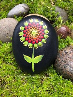 a painted rock with a flower on it sitting in the grass next to some rocks