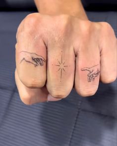 two fingers with the creation of man and woman tattoos on them, one is pointing at another hand