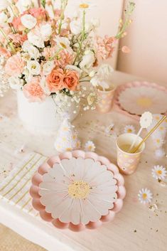 a table topped with pink and white plates next to a vase filled with flowers on top of a wooden table