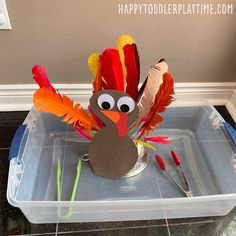 a turkey made out of paper sitting on top of a plastic container filled with feathers