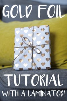 a gift wrapped in white and gold foil sitting on top of a gray couch with yellow pillows