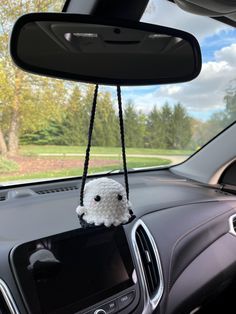 a small stuffed animal hanging from the dashboard of a car with trees in the background