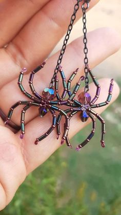 a hand holding a small spider necklace in it's left hand, with purple and blue beads hanging from the back