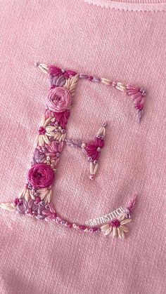 the letter e is made up of flowers and beads on a pink shirt with white thread