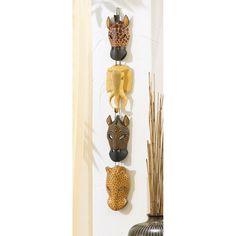 three african masks are hanging on the wall next to a vase with reeds in it