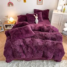 a bed with purple comforter and pillows in a room next to a white rug