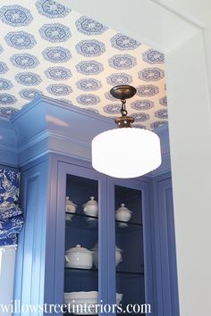 a china cabinet with blue and white wallpaper on the ceiling, next to a light fixture