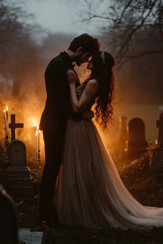 a bride and groom kissing in front of a cemetery at night with candles lit up behind them