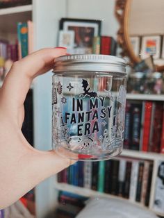 a person holding up a glass jar in front of a book shelf filled with books