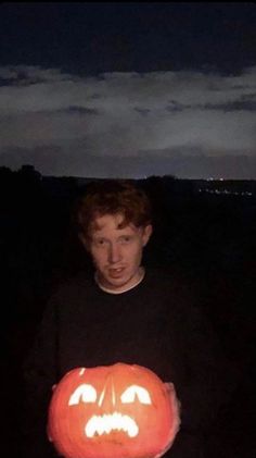 a young man holding a pumpkin shaped like a jack - o'- lantern at night