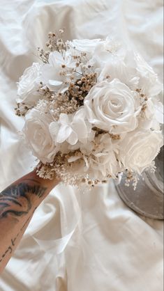 a person holding a bouquet of white flowers on top of a bed covered in sheets