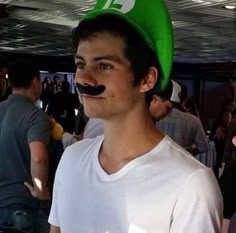 a man wearing a green hat and mustache in front of other people at an event