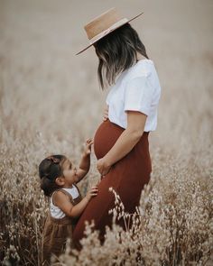 a pregnant woman holding her child's hand while standing in the middle of a field