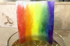 a rainbow colored candle is in a glass holder