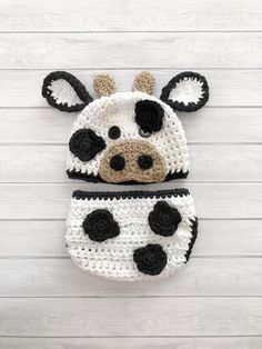 a crocheted cow hat and diaper cover on a white wooden background with planks