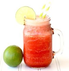 a red drink in a mason jar with lime and straws on the rim next to it