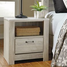 a nightstand with a plant on top of it next to a bed