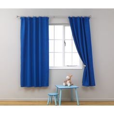 a teddy bear sitting on a small table in front of a window with blue curtains