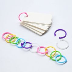 several different colored plastic rings on top of each other next to a white card and some paper clips