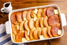 a casserole dish with slices of apple and cheese in it next to a cup of coffee