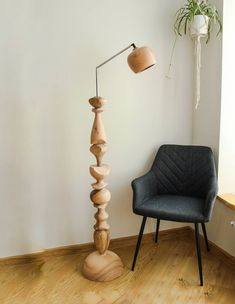 a wooden floor lamp next to a chair and potted plant in a room with white walls