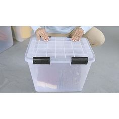 a woman kneeling down with a plastic box on her lap and one hand over the lid