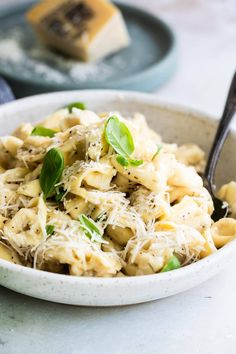 a white bowl filled with pasta covered in cheese and greens next to a slice of cake