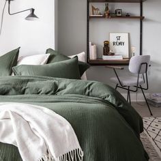 a bed with green comforter and pillows in a bedroom next to a desk area