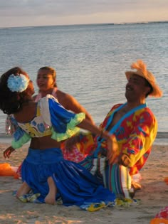 two women dancing on the beach with an ocean in the backgroung and one woman wearing a colorful dress