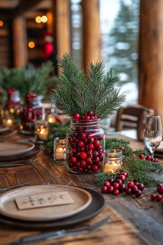 the table is set for christmas dinner with candles and greenery in mason jars on it