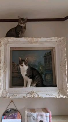 a cat sitting on top of a shelf in front of a framed painting above it