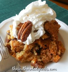 a close up of a piece of cake on a plate with whipped cream and pecans