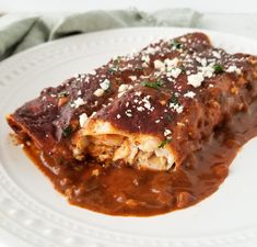 a white plate topped with enchilada covered in sauce