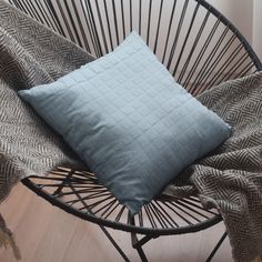 a blue pillow sitting on top of a black chair next to a gray and white blanket