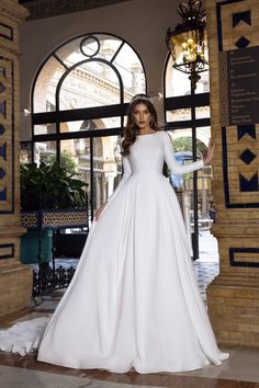 a woman standing in front of a doorway wearing a white dress and long sleeved top