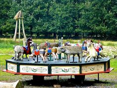 a carousel with horses and people on it in the middle of an open field next to trees