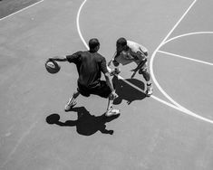 two men playing basketball on an outdoor court with shadows from the sun shining on them