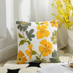 a yellow and green flowered pillow sitting on top of a rug next to a window