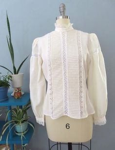 Vintage 80's Victorian blouse. Off white silk with high lace ruffle collar, eyelet lace, horizontal pleats and button lace cuffs. Button down back with billowy long sleeves with puffed shoulders. Sightly sheer overall. Straight hem. Gorgeous top would be great for a formal event.  Fits up to a size large. Please double-check the measurements below: MEASUREMENTS--Taken with garment laying flat, in inches, doubled: Bust: 40"  Waist: 38"  Shoulder: 14" Length: 23" {top neck to bottom hem} Neck: 14" Sleeve length: 24.5" Label/ Era: Royal Silk | 1980 Stated Size: 8 Fabric: Silk, acrylic buttons Condition: Excellent condition. Freshly laundered. No known issues.  ★ Shop entire shop here: https://www.etsy.com/shop/retrosuzysvintage Instagram | retrosuzysvintage Facebook | retrosuzysvintage Pinter Fitted Long Sleeve Lace Top, Elegant Lace Patchwork Blouse For Fall, Elegant Fall Blouse With Lace Patchwork, Fitted Lace Trim Top For Work, Feminine Fitted Fall Blouse, Formal Fall Lace Top, Formal Long Sleeve Lace Top For Fall, Formal Lace Top With Lace Trim For Fall, Elegant Fitted Lace Top For Fall