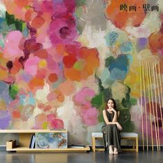 a woman sitting on a bench in front of a colorful wall with flowers painted on it