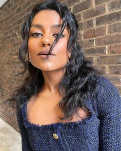 a woman standing in front of a brick wall wearing a blue sweater and gold earrings