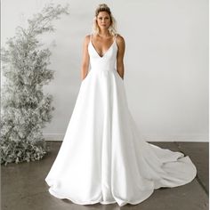 a woman standing in front of a white wall wearing a wedding dress with spaghetti straps