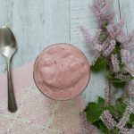 a spoon and some purple flowers on a white wooden table next to a pink napkin