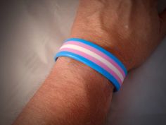 a person wearing a bracelet with pink and blue strips on it's wrist,