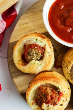 some meatball rolls are on a wooden plate with sauce and a small white bowl