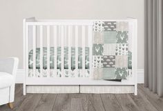 a white crib with a green and gray quilted blanket next to a chair