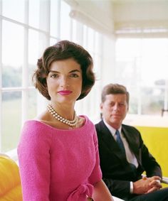 a woman wearing a pink dress and pearls sits next to a man in a suit