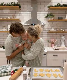 a man and woman holding a baby while standing in front of a counter with cookies on it